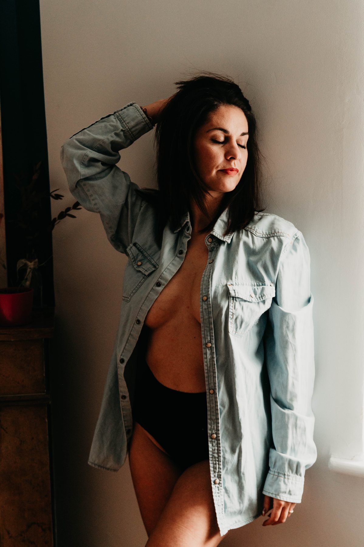 Chemise en jean ouverte sur lingerie, près de la fenêtre, regard complice