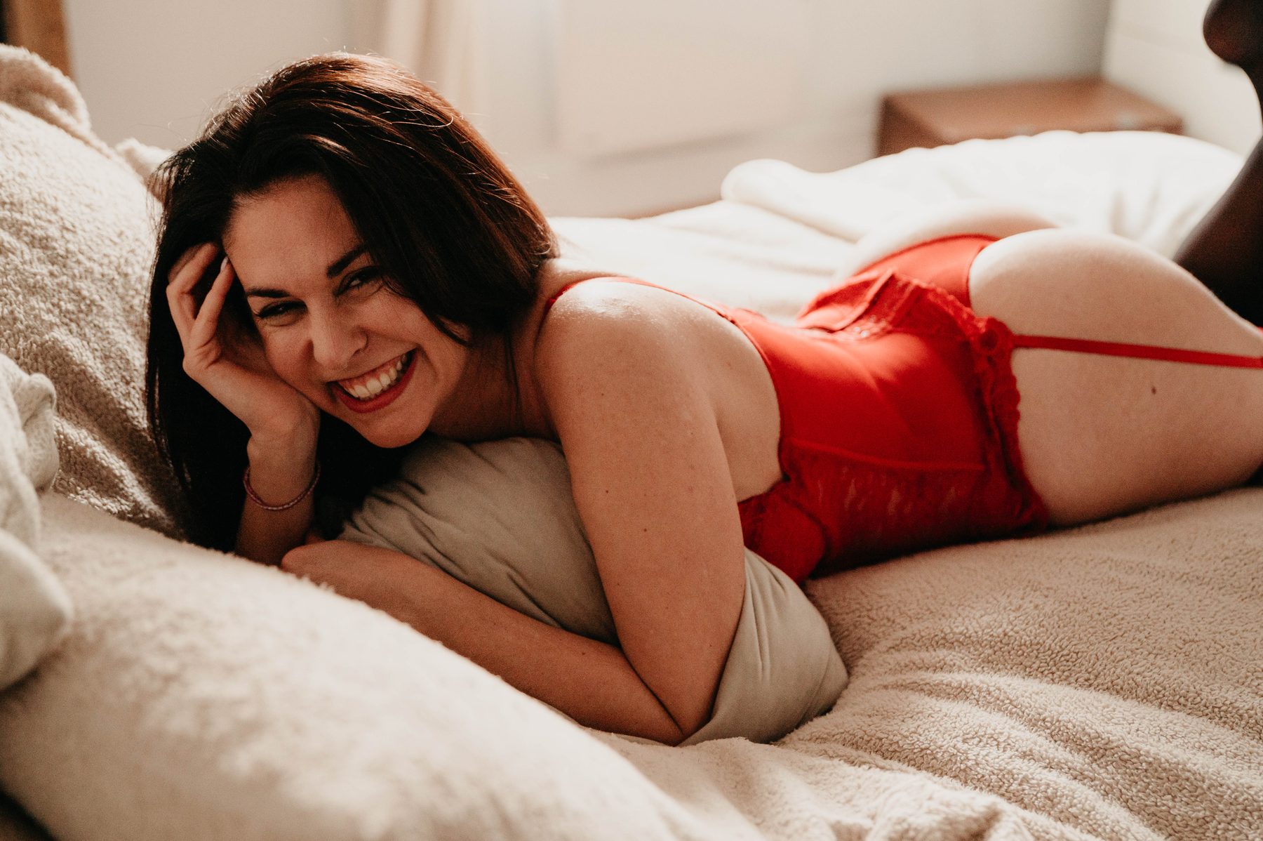 Femme allongée sur le lit, sourire détendu, lumière chaude et bienveillante